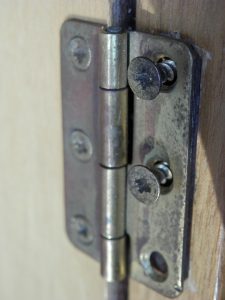 Closeup of a door hinge with loose screws.